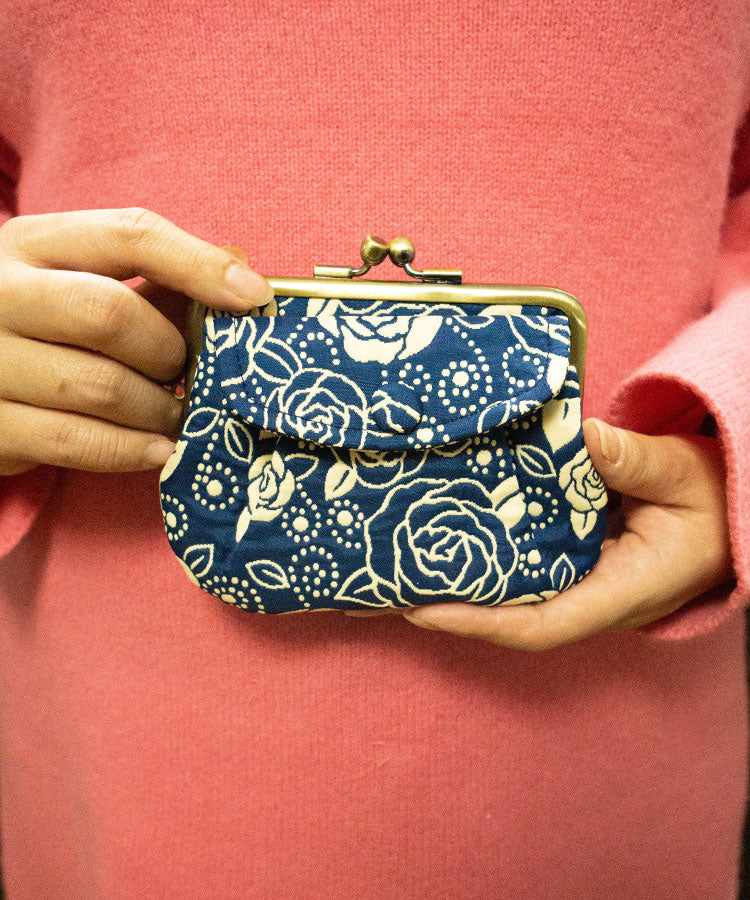 Person holding a blue floral patterned japanese coin purse against a pink background