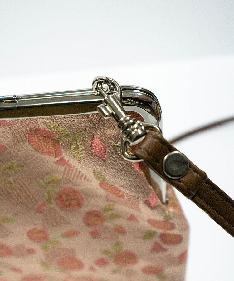 Close-up of a handbag with floral pattern and brown strap on a white background